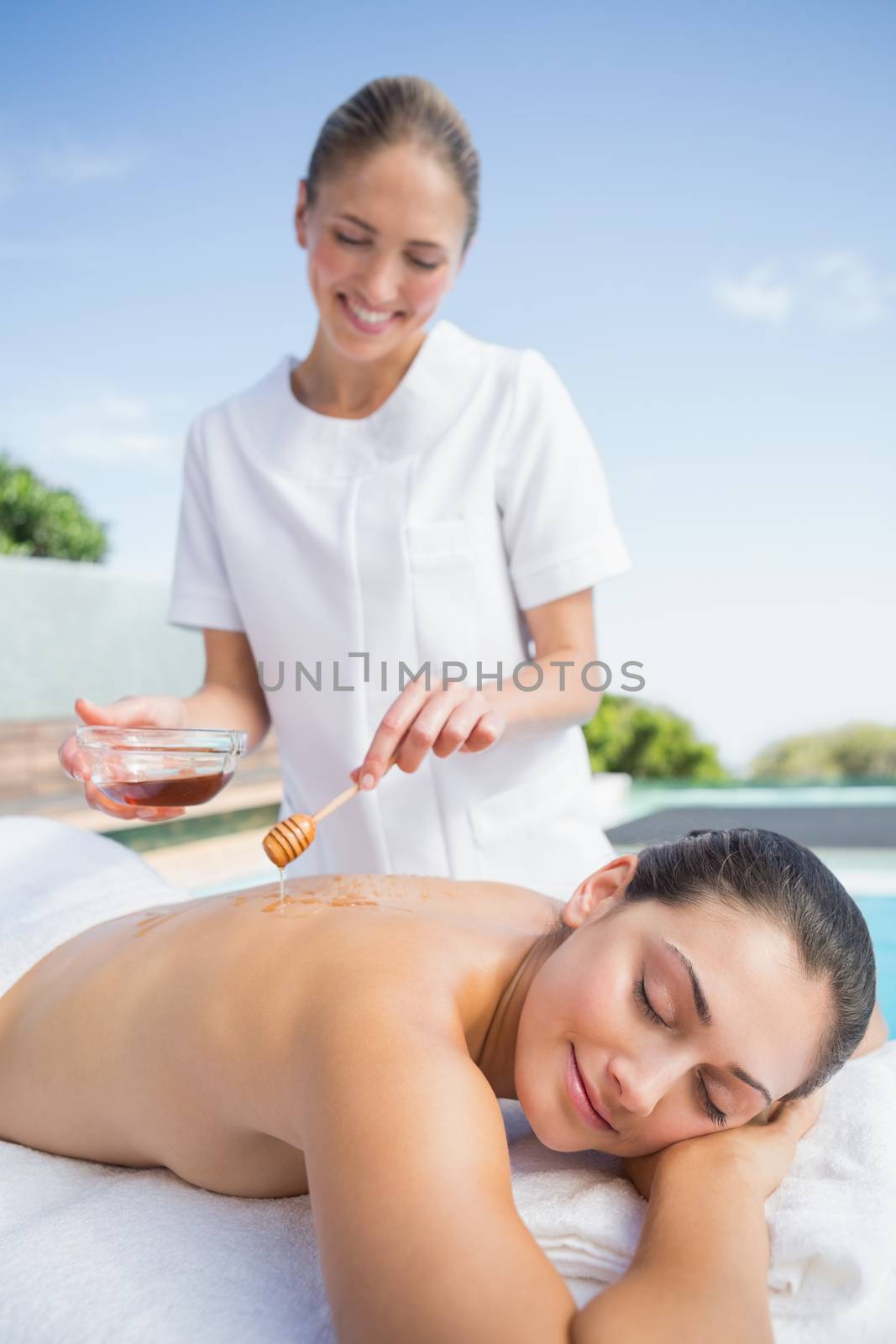 Happy brunette getting a honey beauty treatment poolside by Wavebreakmedia