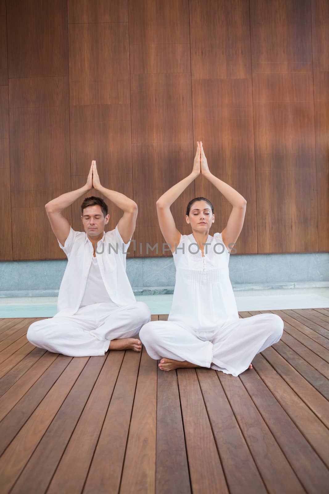 Attractive couple in white sitting in lotus pose with hands together by Wavebreakmedia