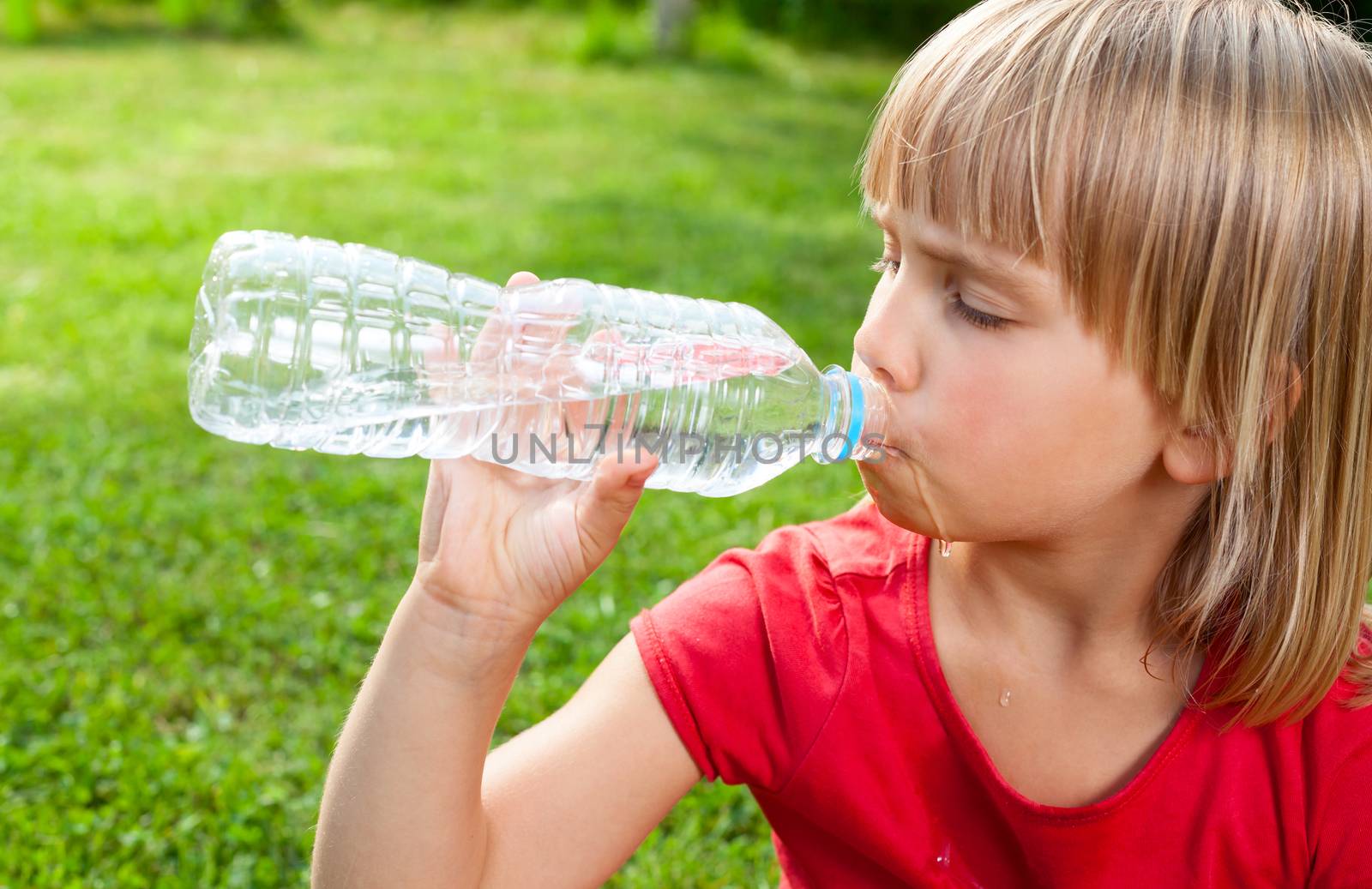 Cute little girl drinking water in a summer garden