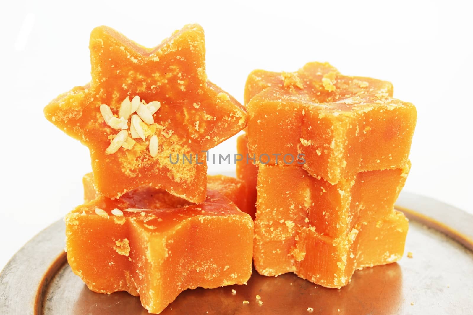 Hard molasses or jaggery derived from sugarcane juice, in star shape and garnished with melon seeds. Also known as gur, it is preferred as a healthier sweetener across Asia, as against white sugar. Usable in culinary and health concepts.
