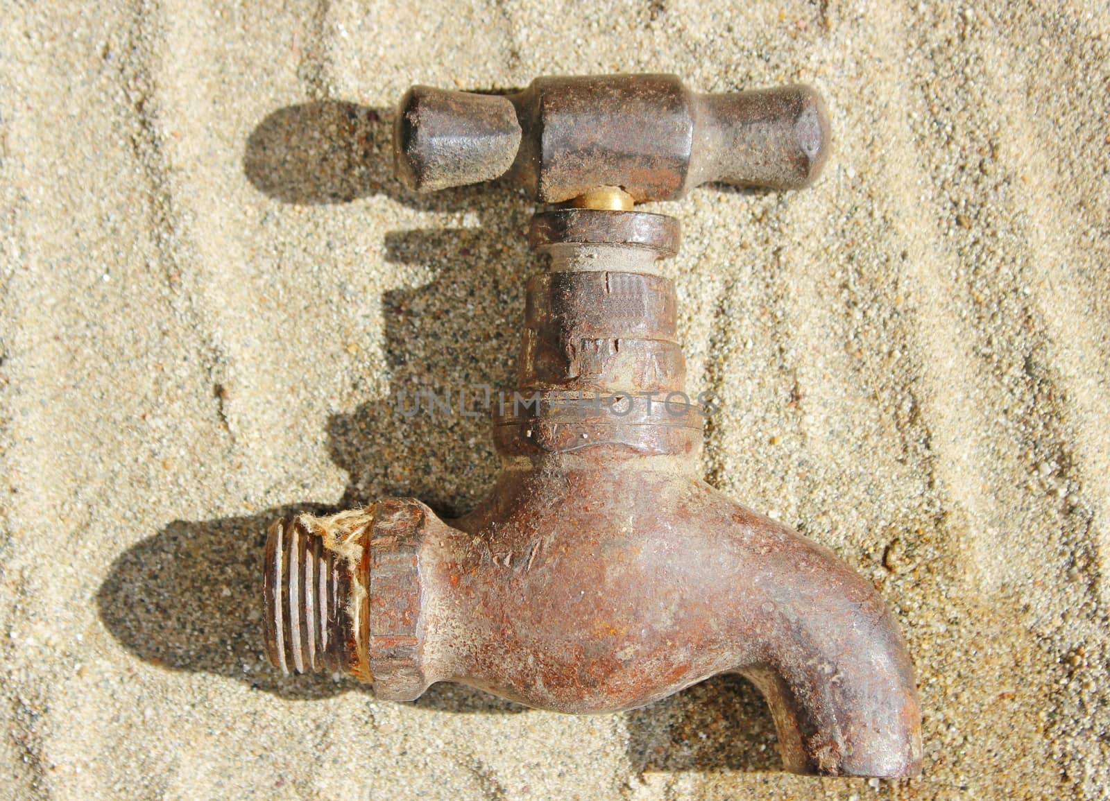 An old brass water tap or faucet, lying on sand. Ideal for use in water scarcity or save water concept.
