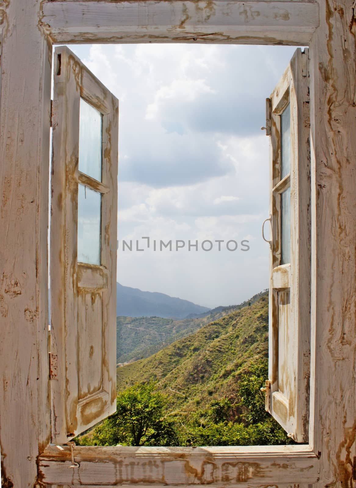 View of the mountains and clouded sky from an open old white wood window. Ideal for concepts related to outdoors, nature, exploration, peace, and inspiration.
