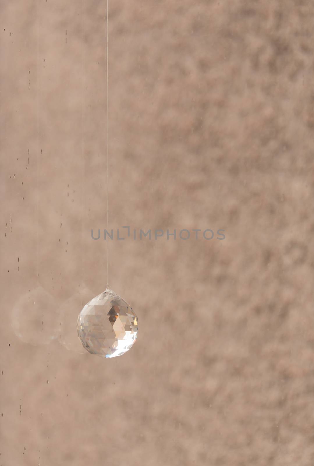 Crystal ball hanging in rainy window with rough cast wall behind. Interior detail.