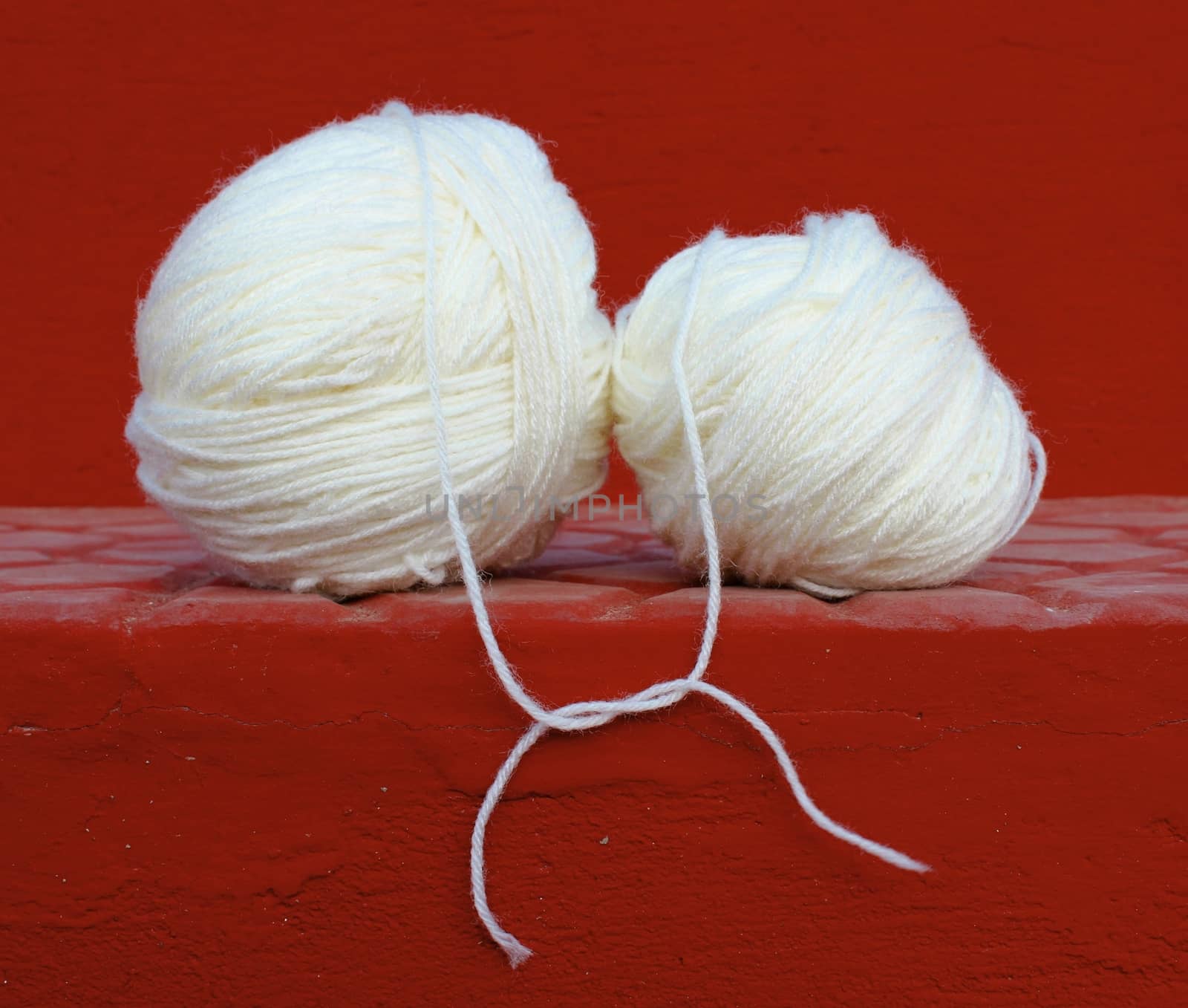 Two white wool yarn balls with their treads tied up in a knot, shot against a red concrete steps background. It can be used for relationship concepts like -love, togetherness, connection, and for business concepts like - mergers, joint venture etc. 

