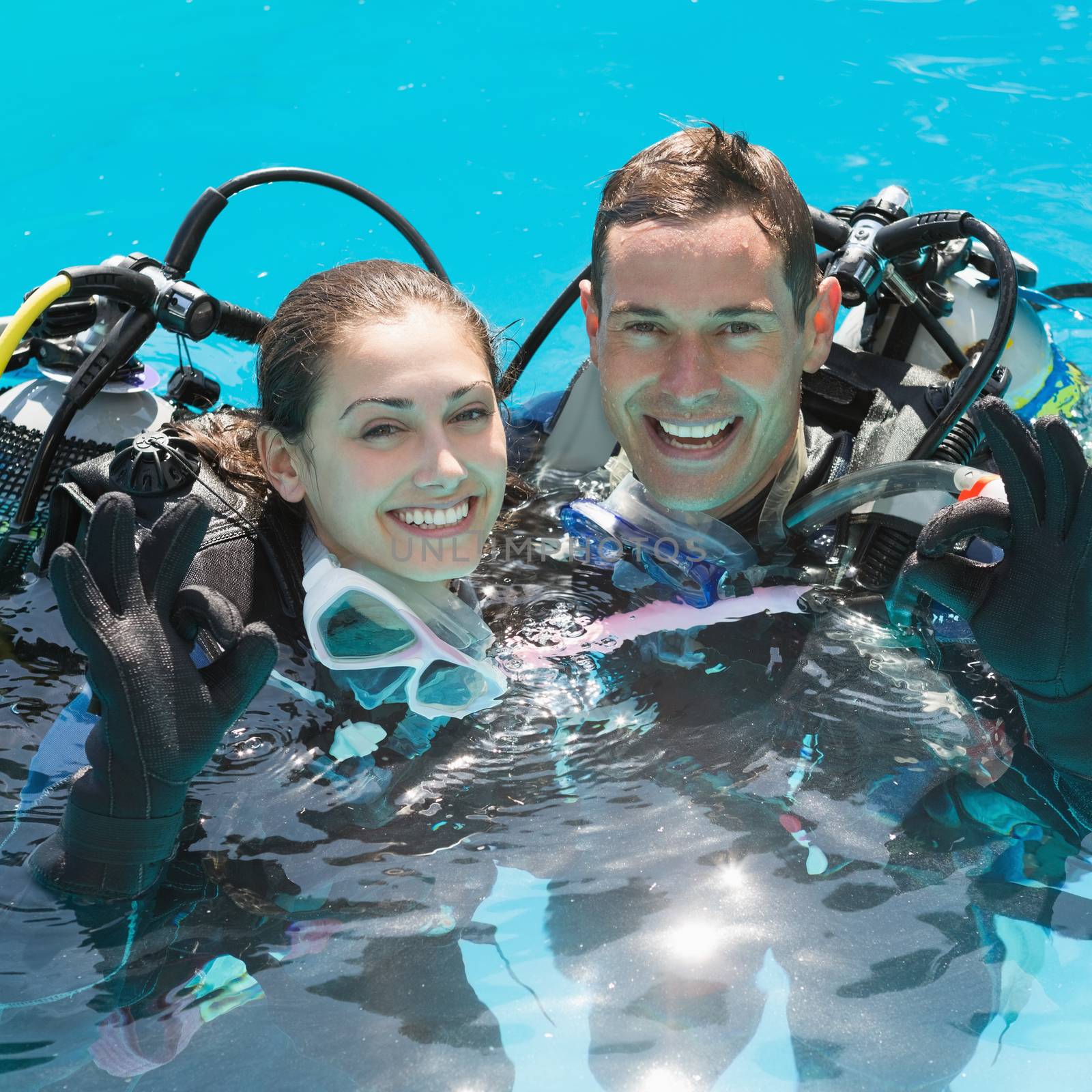 Smiling couple on scuba training in swimming pool showing ok gesture on a sunny day