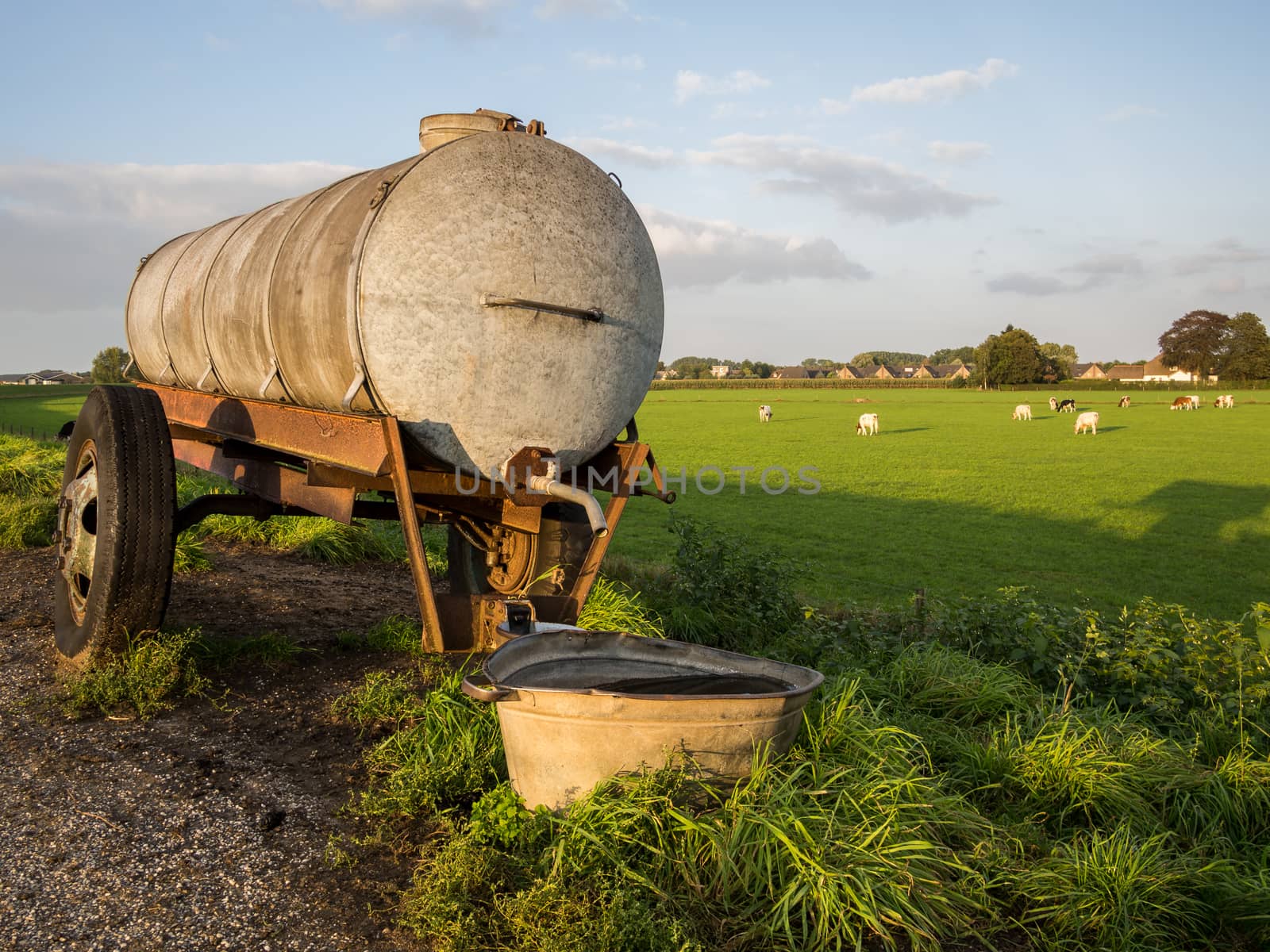 Water tanker by meadow during sunset by frankhoekzema