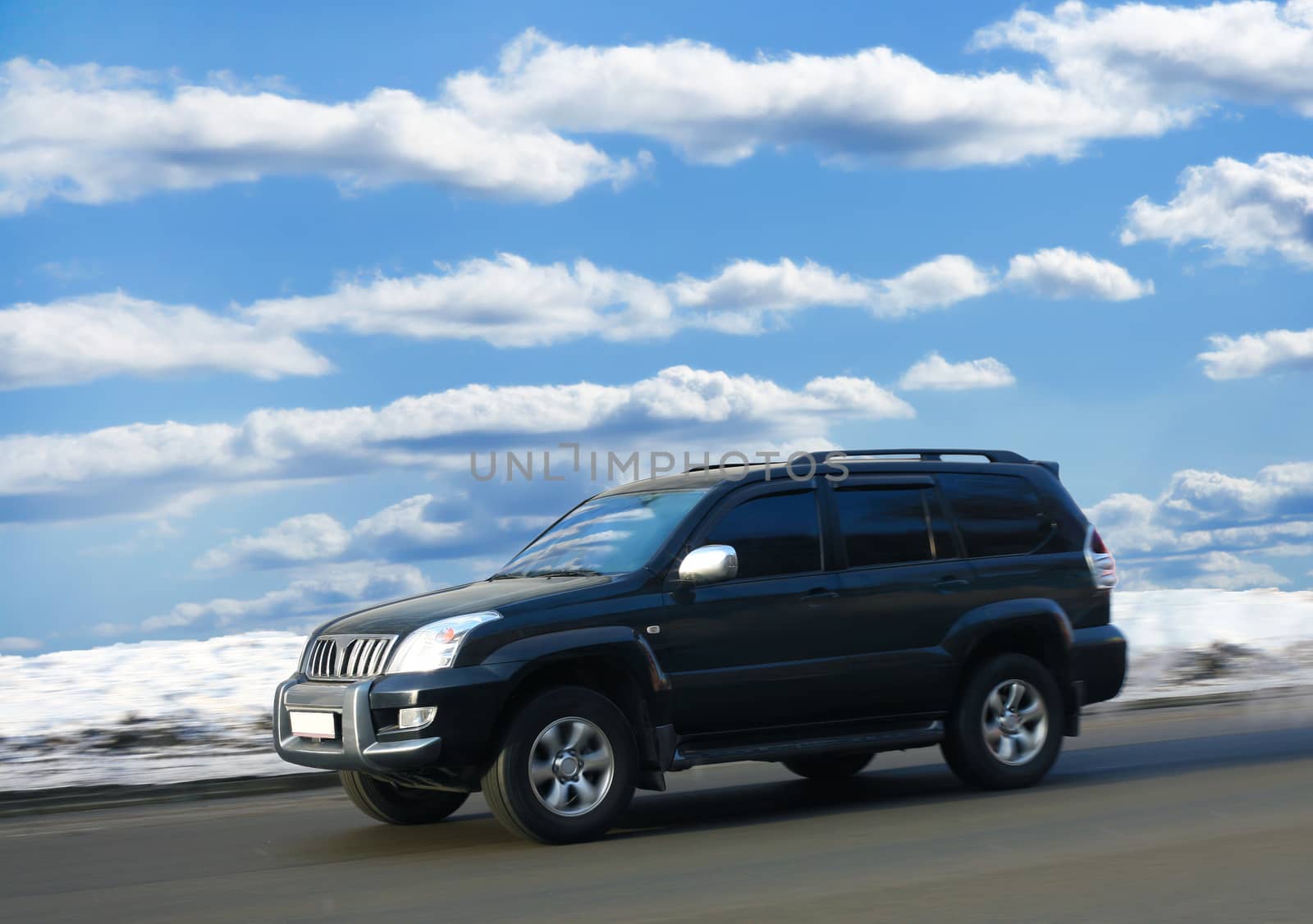 SUV goes on winter road against clear cloudy sky