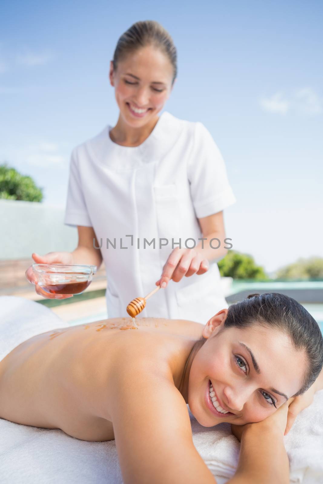 Happy brunette getting a honey beauty treatment poolside outside at the spa