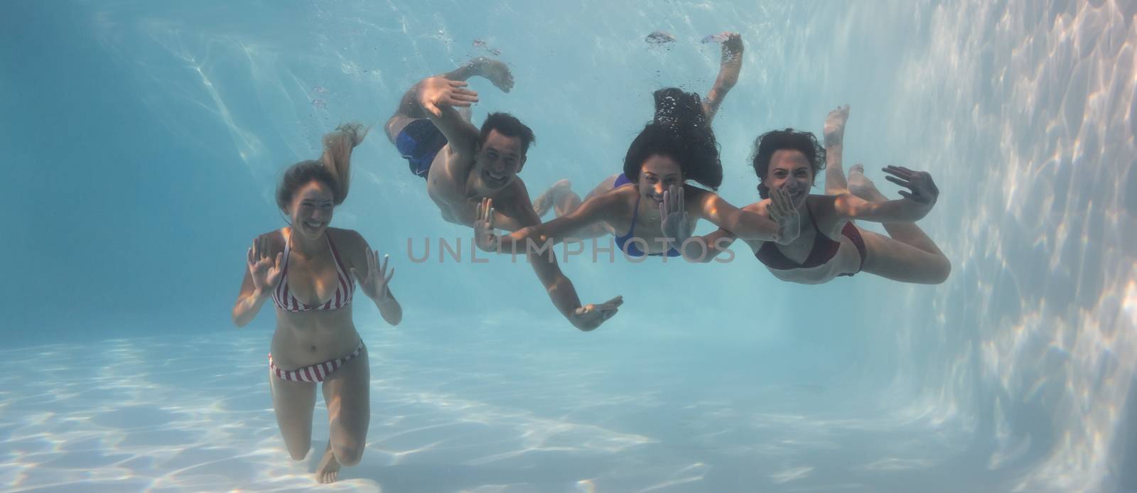 Smiling friends looking at camera underwater in swimming pool by Wavebreakmedia