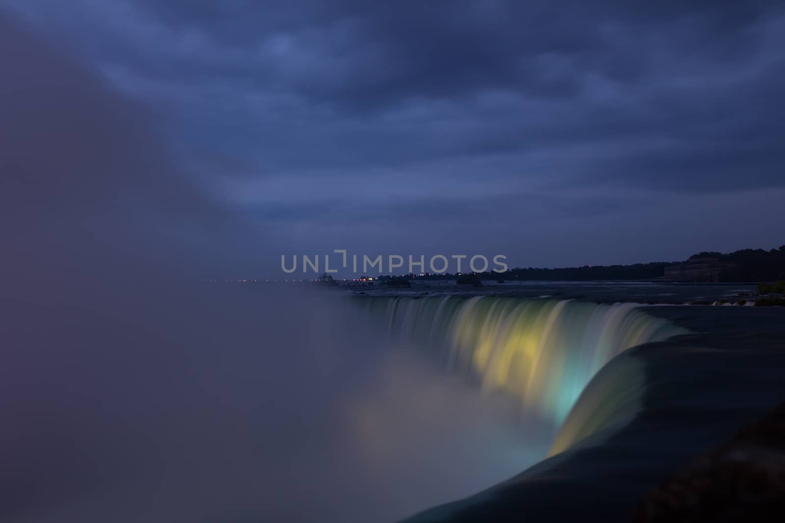 Niagara Falls lit at night by colorful lights, smoke water