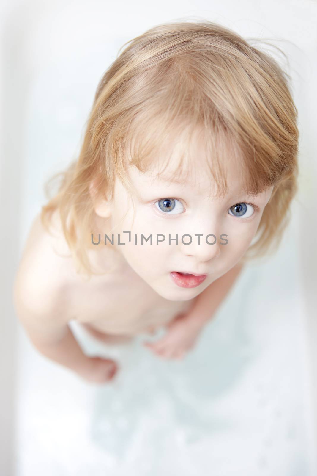 boy with long blong hair standing in bathtub looking up