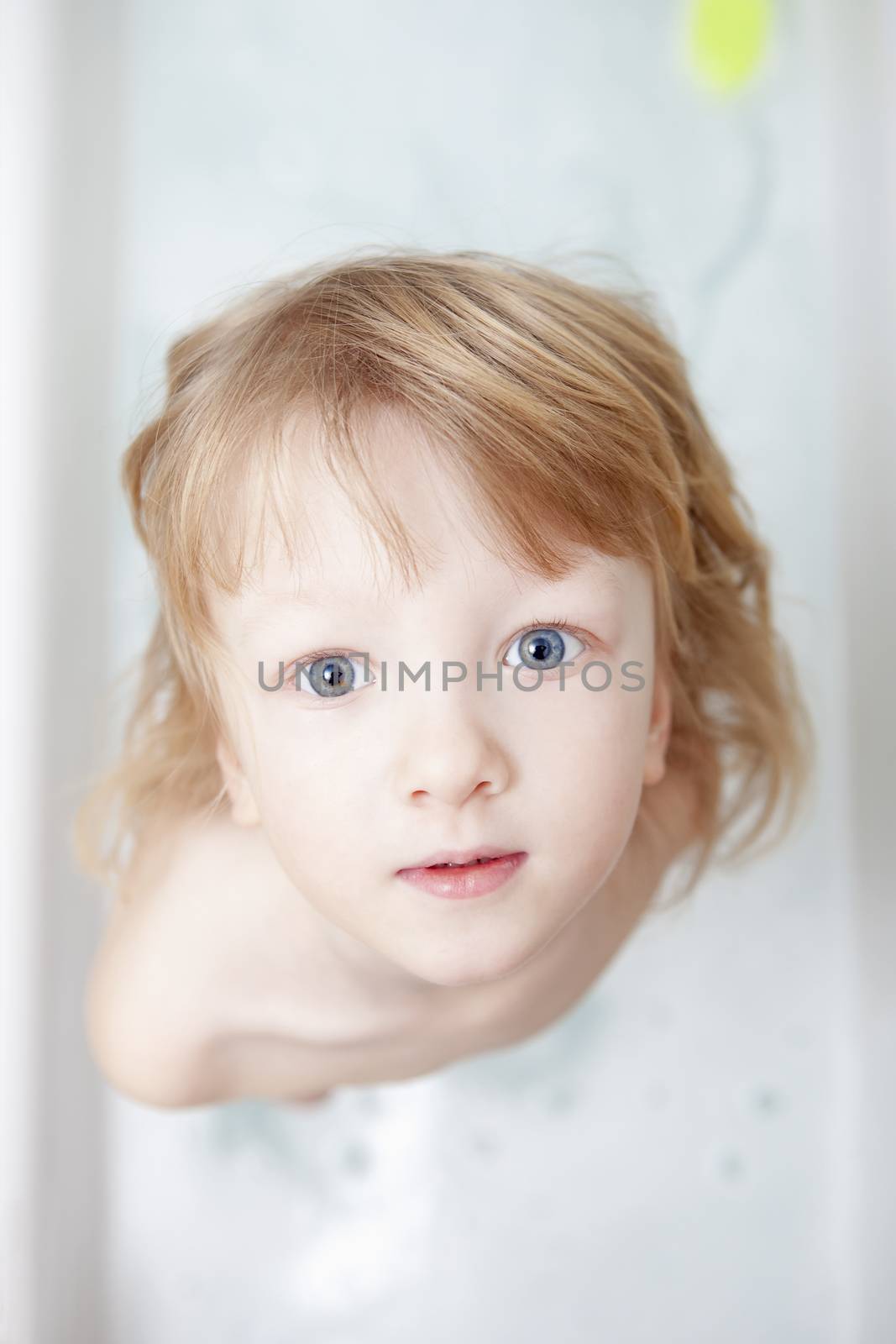 boy with long blong hair standing in bathtub looking up