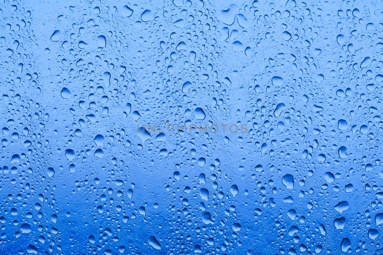 closeup of waterdrops after rain on glass roof reflecting blue sky