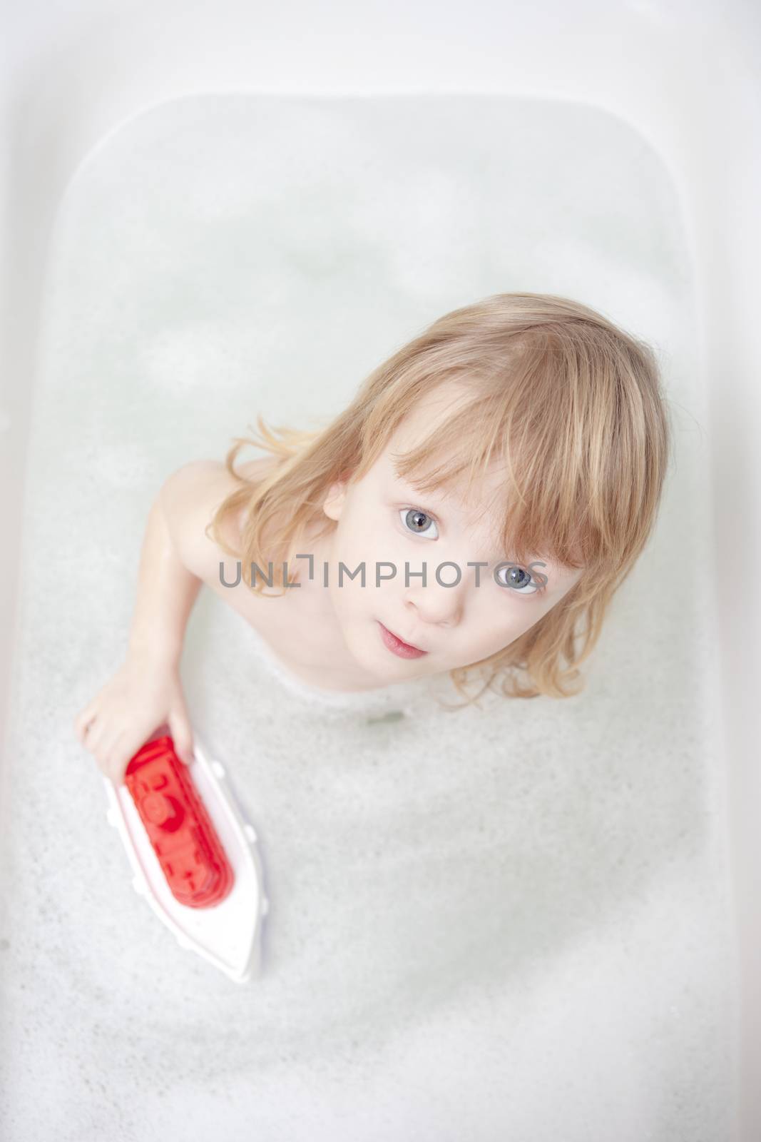 boy with long blond hair playing with plastic boat in bathtub