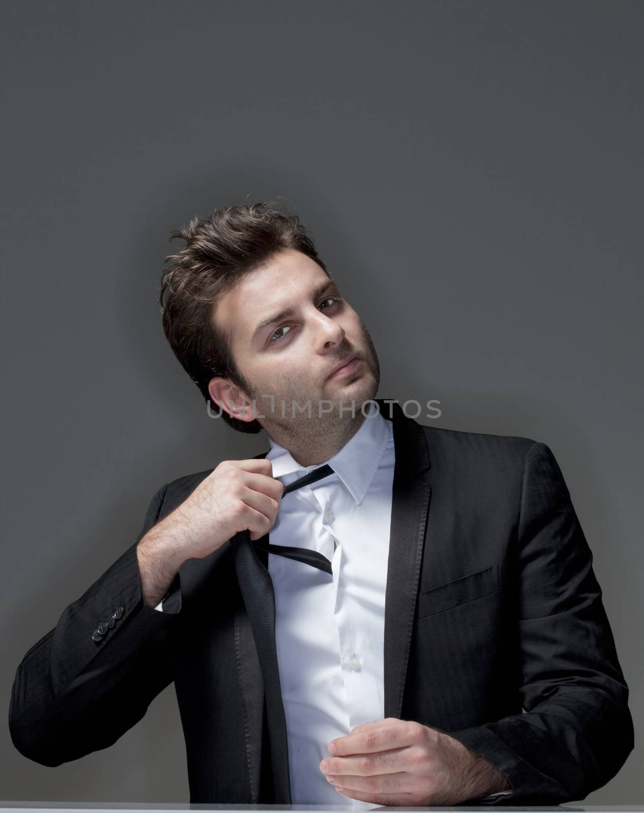 businessman in suit loosening up his tie - isolated on gray