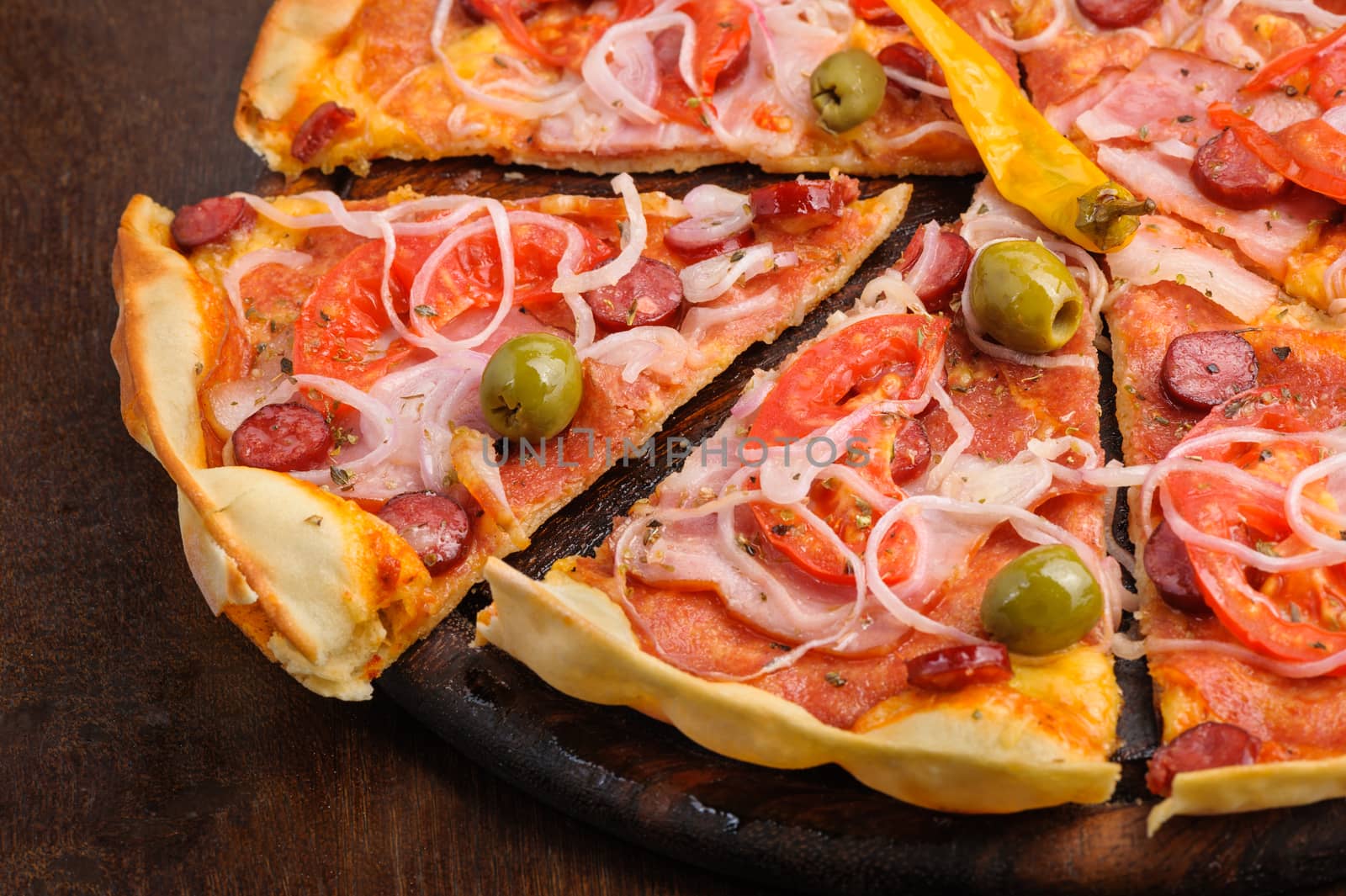 Closeup of pizza with tomato, salami, peppeeoni, olives and yellow hot pepper
