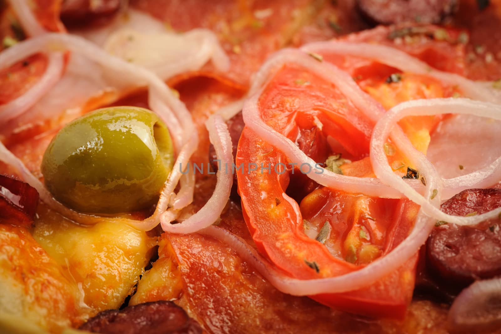 Macro closeup of pizza with tomato, salami, peppeeoni, olives and onion