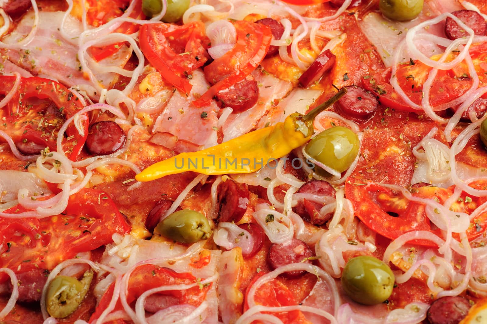 Macro closeup of pizza with tomato, salami, peppeeoni, olives and yellow hot pepper