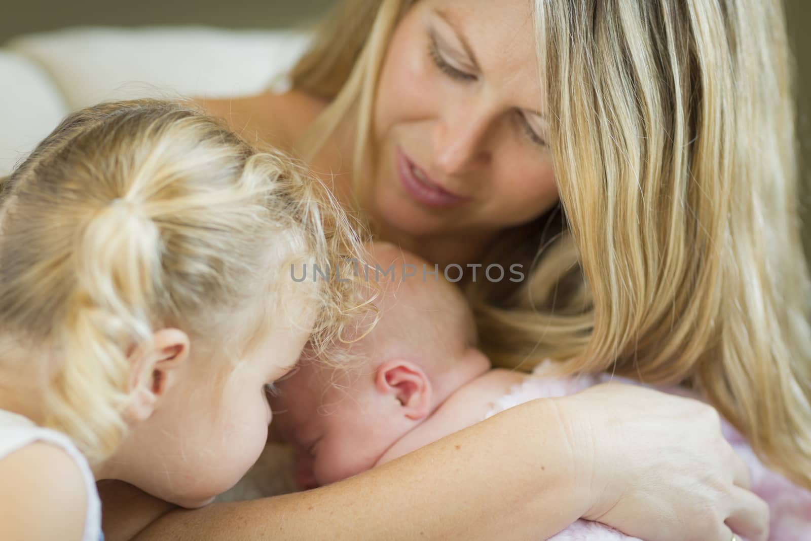 Beautiful Young Mother Holds Newborn Baby Girl as Young Sister Looks On.