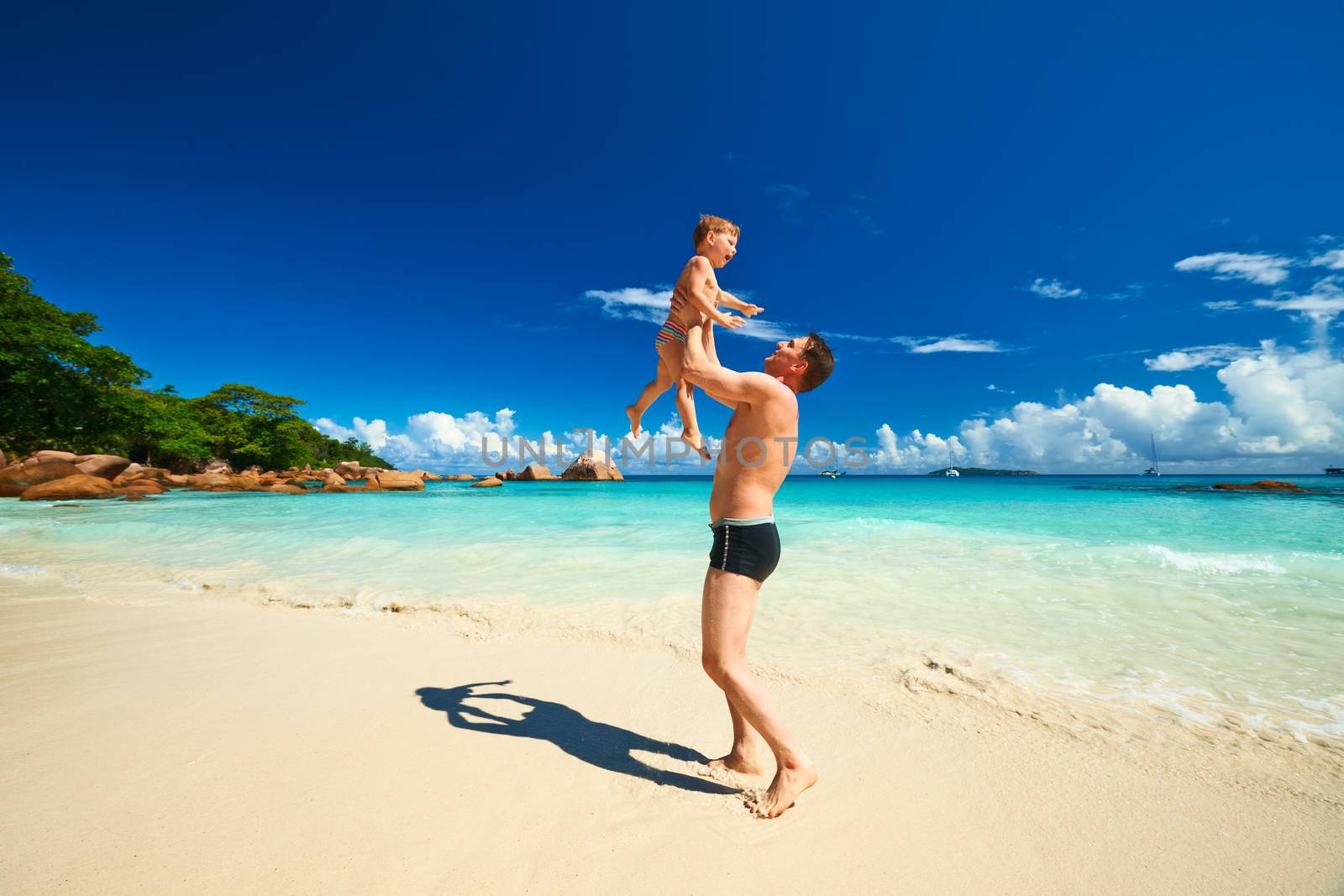 Two year old baby boy and his father playing on beach at Seychelles