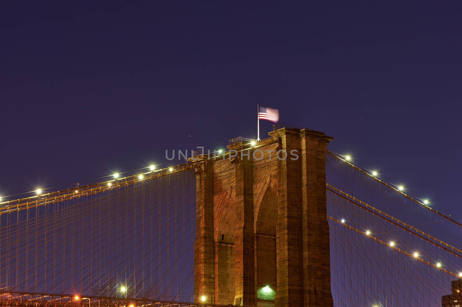 Close up of a pillar of the Brooklyn bridge with flag at night by haveseen