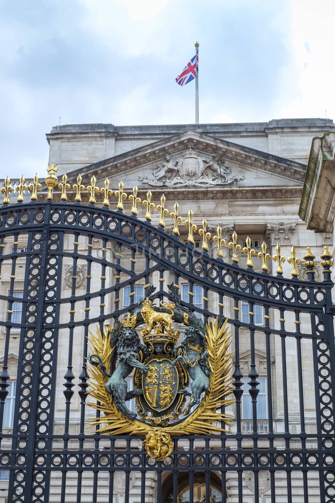 Detail of Buckingham Palace gates with Queen's crest and British flag atop the palace's facade in London, UK