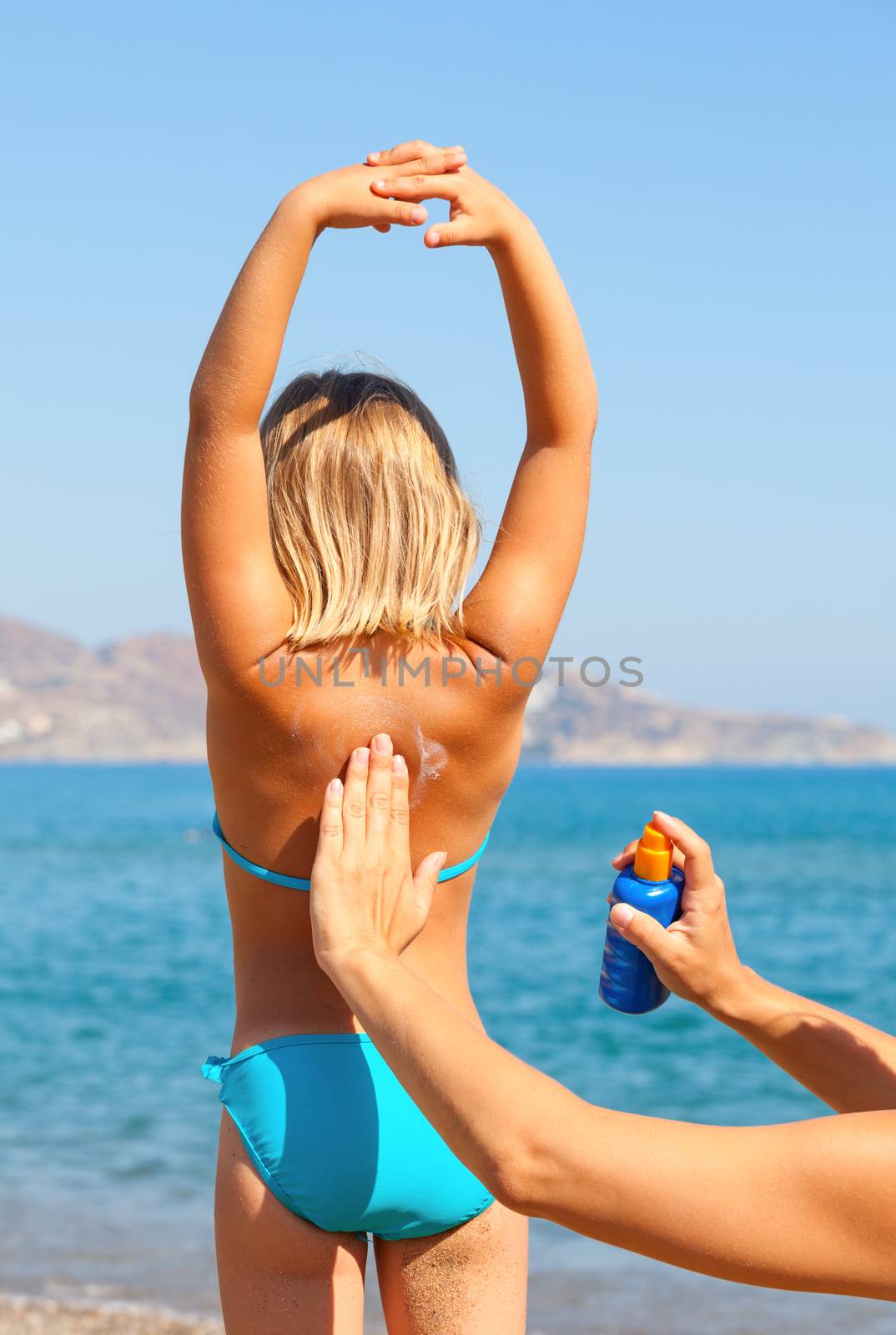 Mother applys sunblock cream on daughter's back