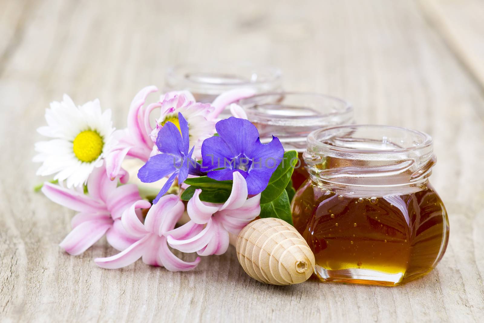 Honey in jars, flowers and honey dipper on wooden background