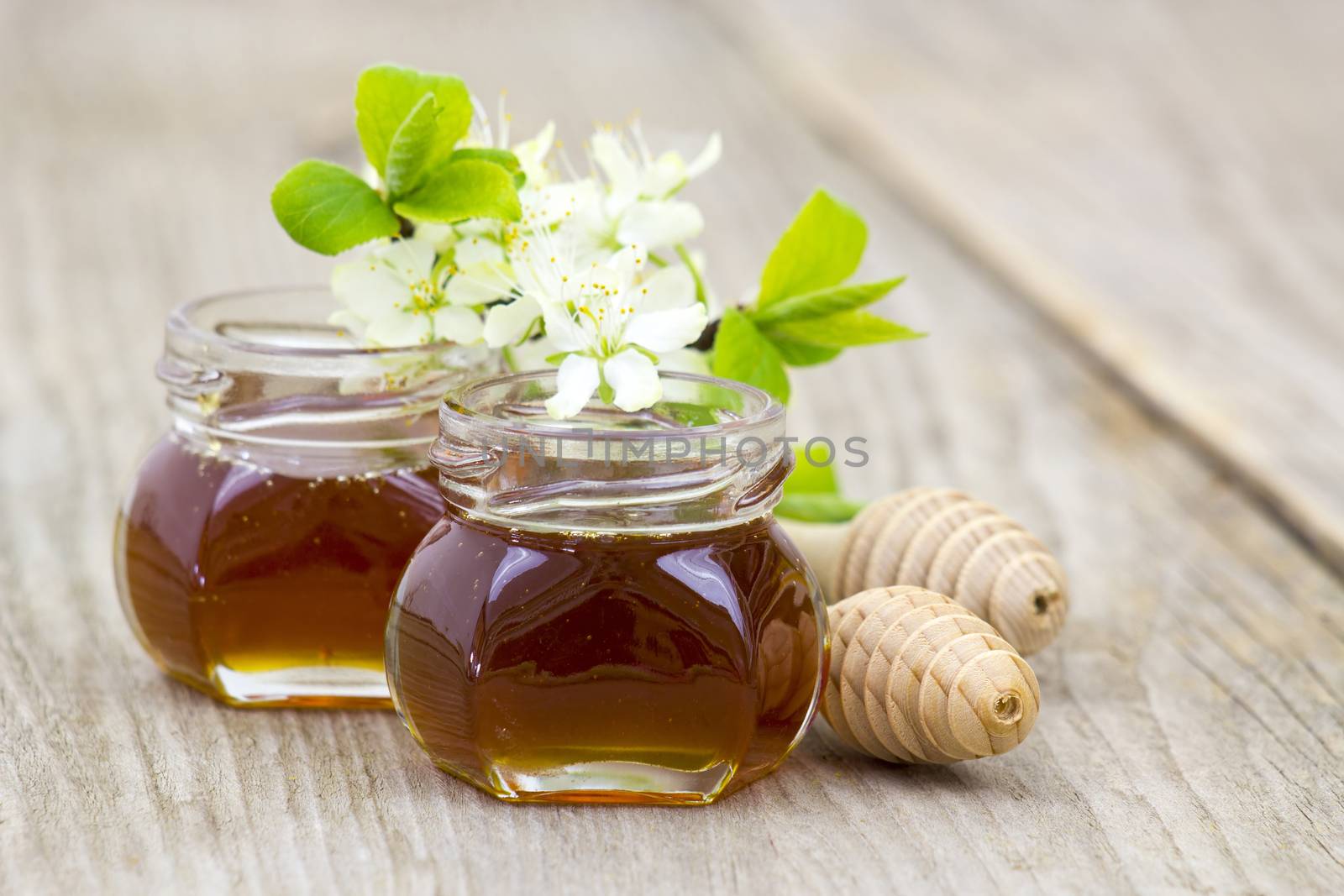 Honey in jars, flowers and honey dipper on wooden background