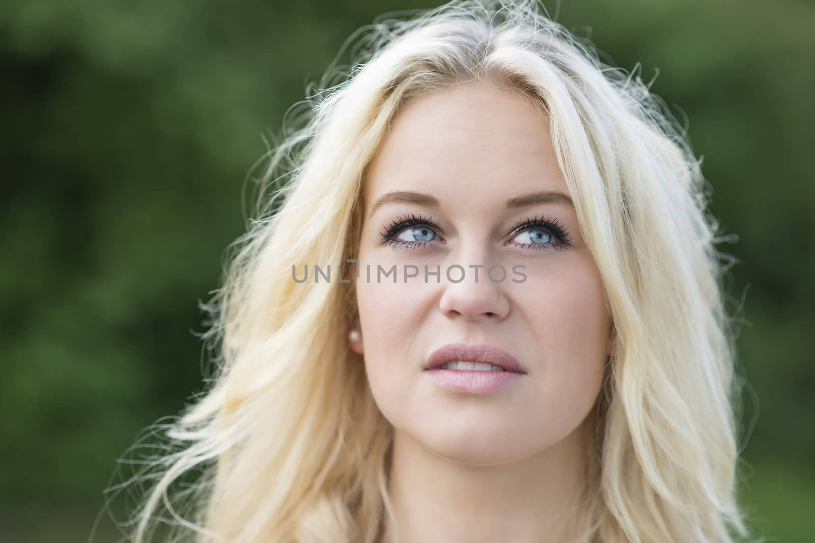 Outdoor portrait of a young blond woman in summer with green background