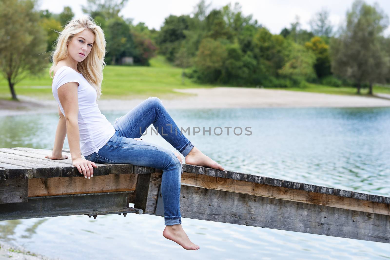 Young blond woman is sitting on a jetty at a lake in summer