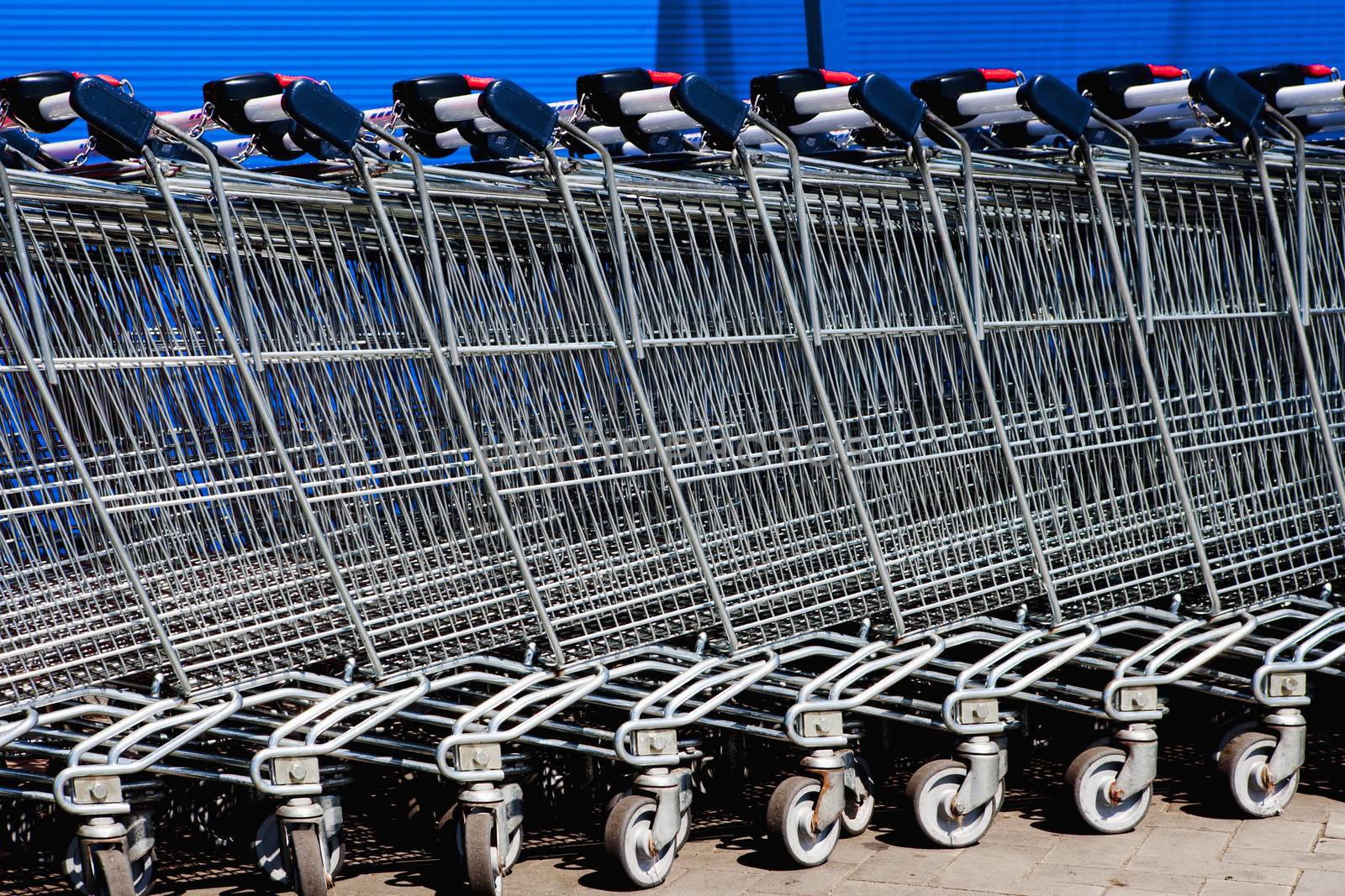 a line of empty supermarket shopping carts against blue wall