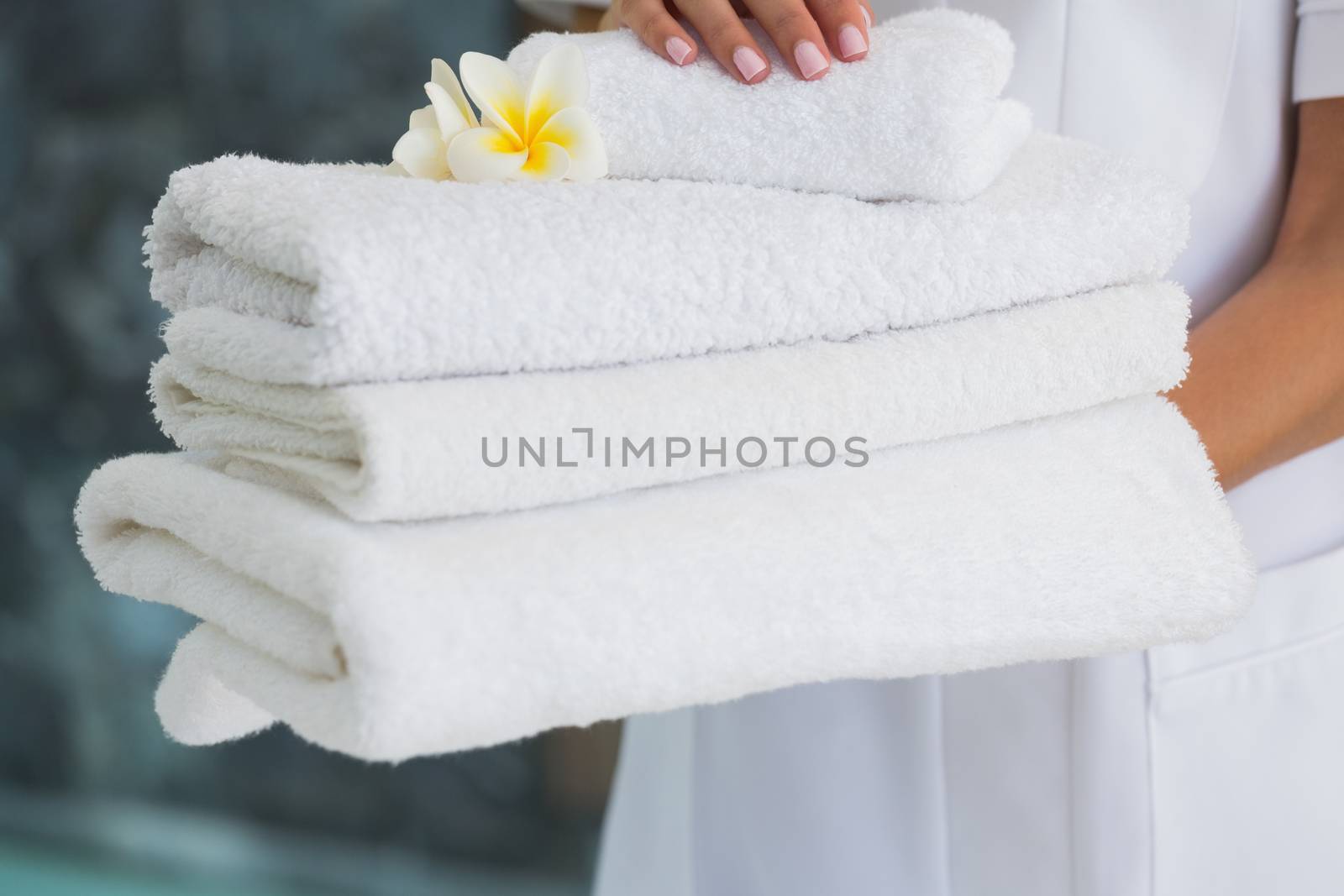Beauty therapist holding pile of fresh white towels at the spa