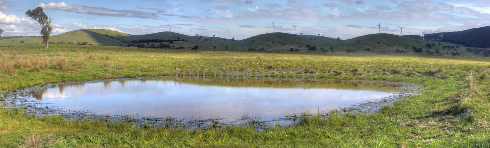 Rural views of picturesque countryside, rolling hills and eco-friendly wind farm and a foreground watering hole