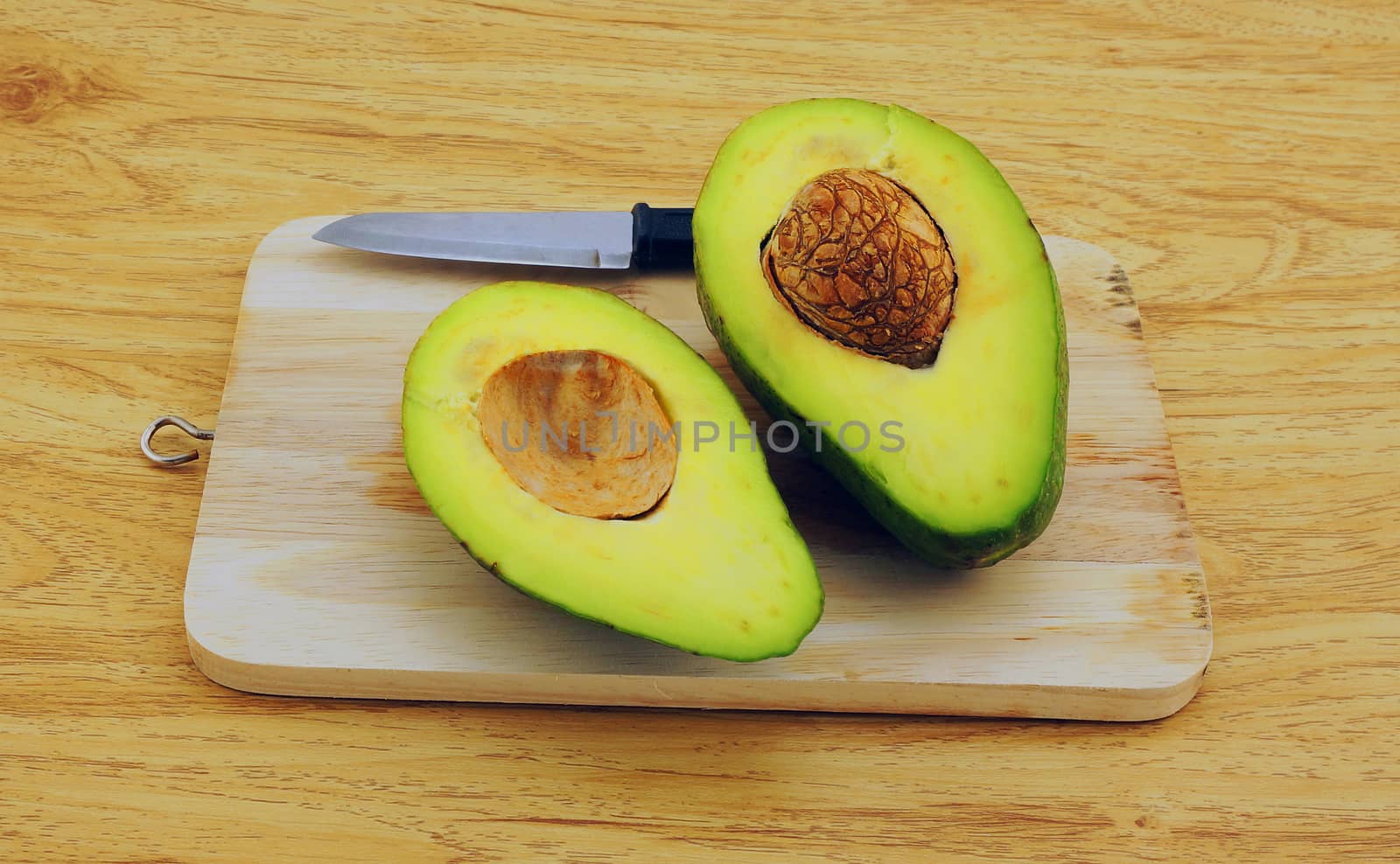 Fresh avocado on cutting board over wooden background, there is a knife placed beside.                               