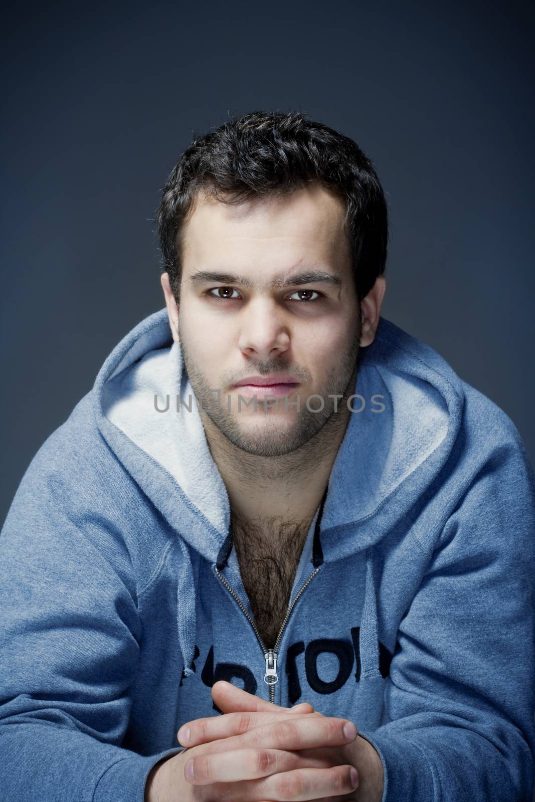 portrait of a young tough man with dark hair - isolated on dark blue