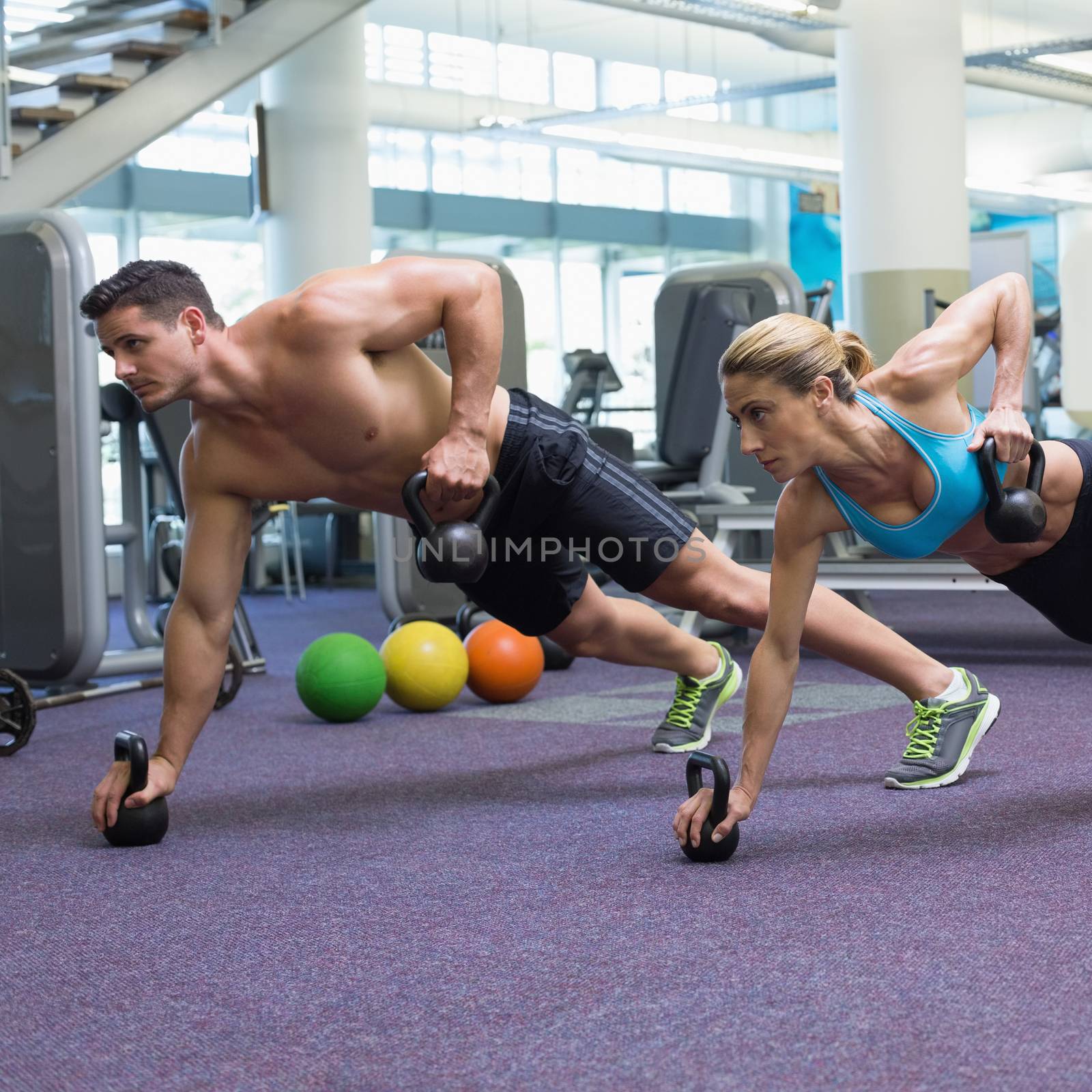 Bodybuilding man and woman lifting kettlebells in plank position at the gym
