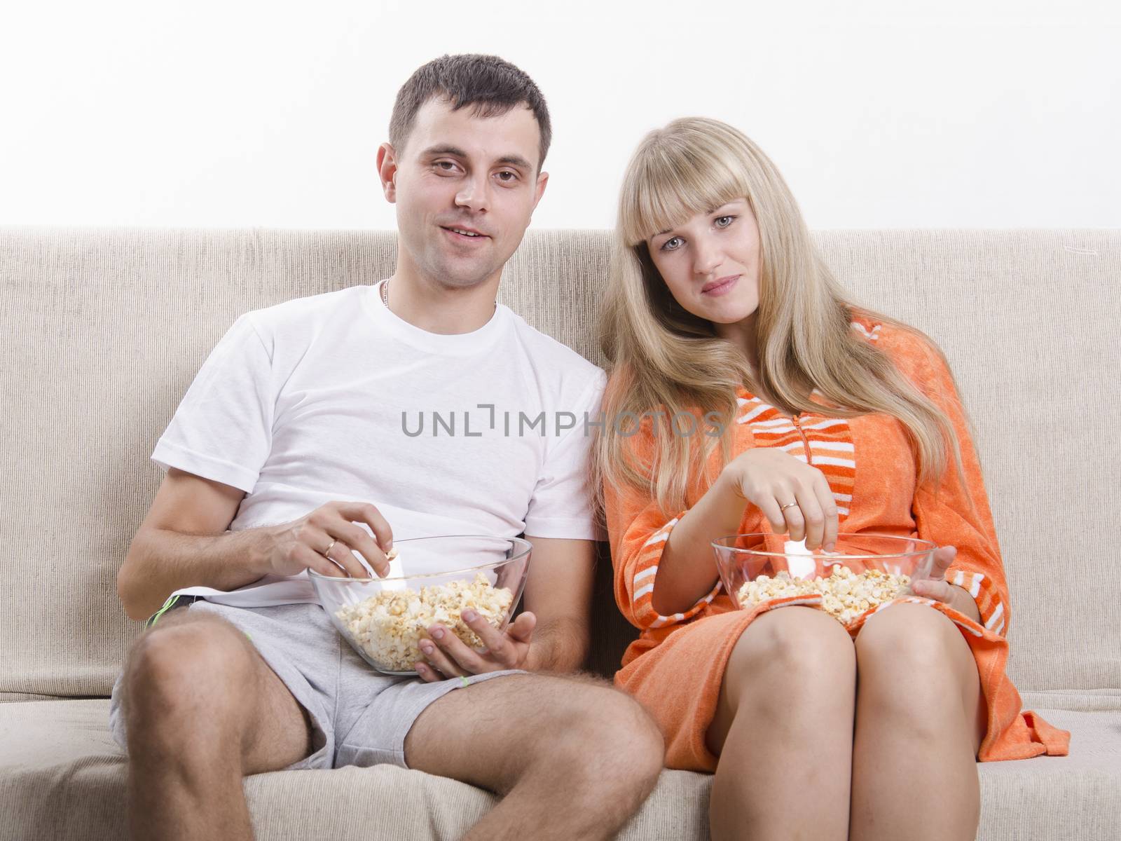 Young couple sitting on couch, eating popcorn and watching TV by Madhourse