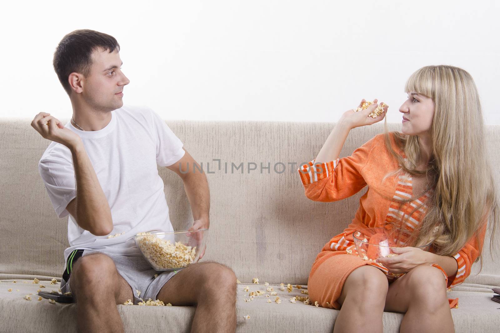 Couple sits on the couch. Each lap Cup of popcorn. Paka throws each other popcorn