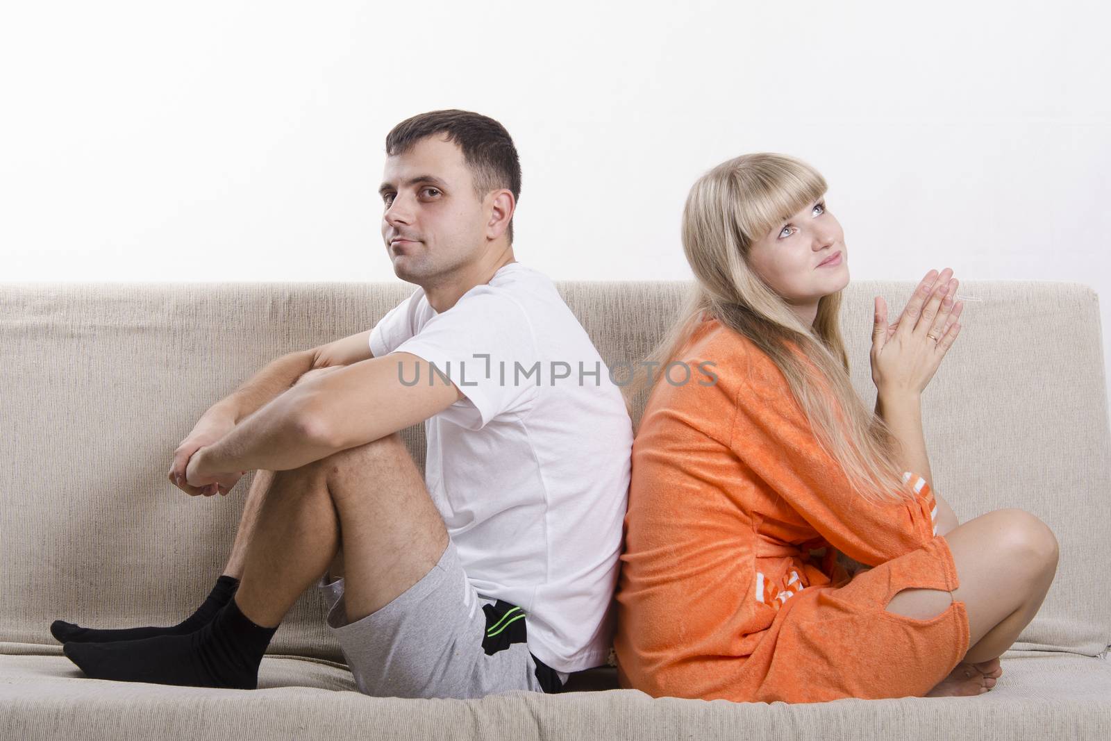 Young couple sitting on the couch, backs to each other. Both dressed in home clothes. The pair dressed in a home.
