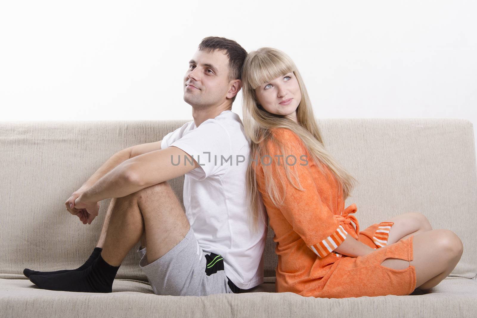 Young couple sitting on the couch, backs to each other. Both dressed in home clothes. The pair dressed in a home.