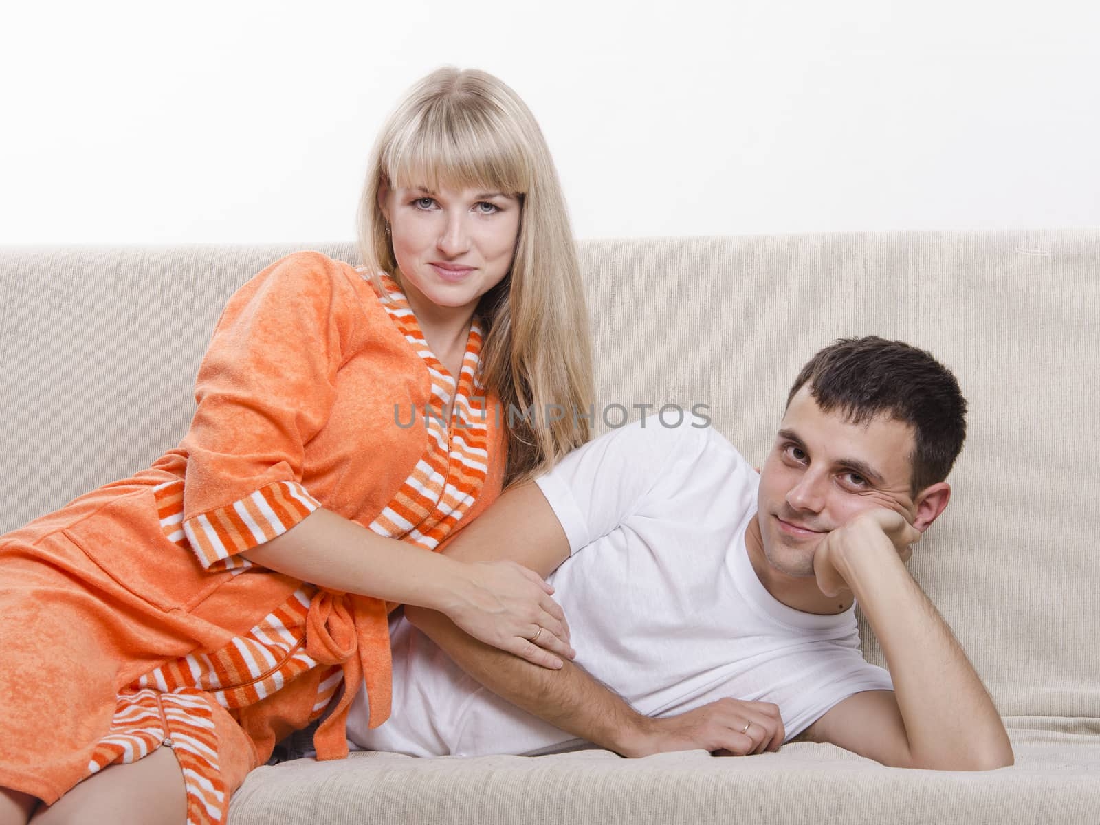 Young couple lying on the sofa and with a smile, looking into the frame.