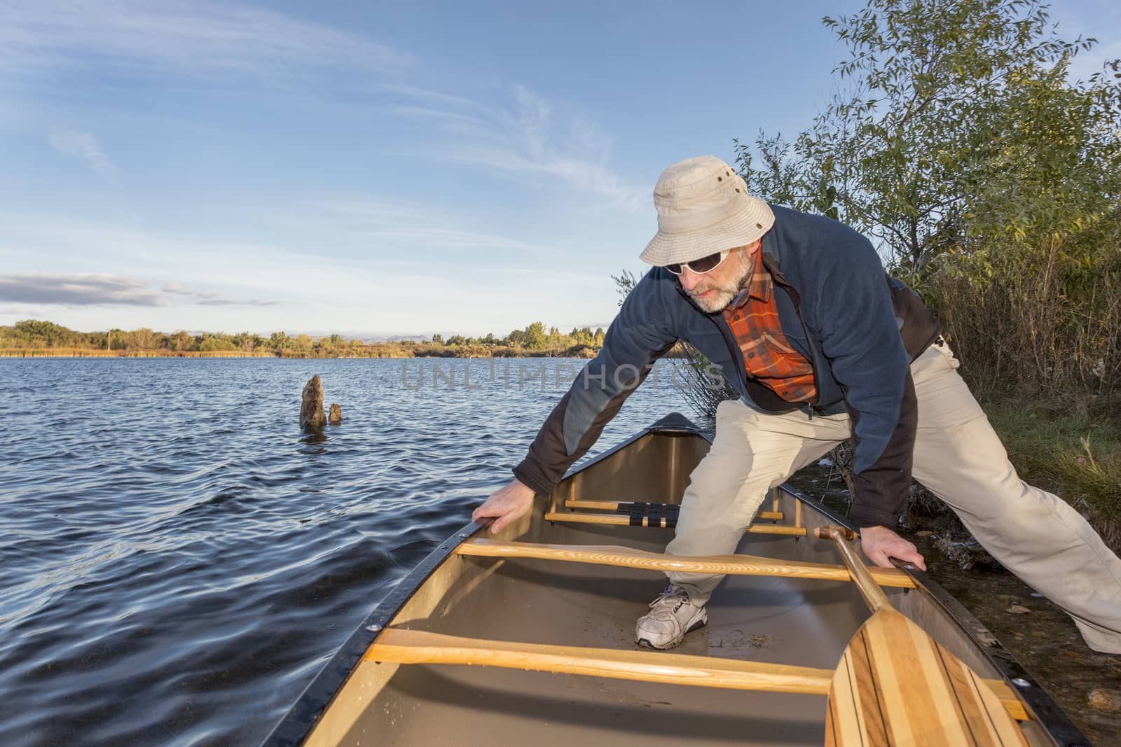 senior male launching canoe for  morning paddling, on a lake Riverbend Ponds Natural Area, Fort Collins, Colorado