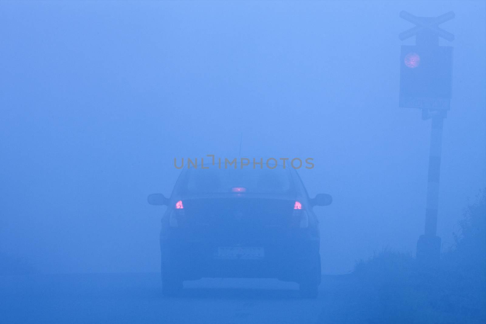 car waiting at rural railroad crossing with red lights blinking in fog
