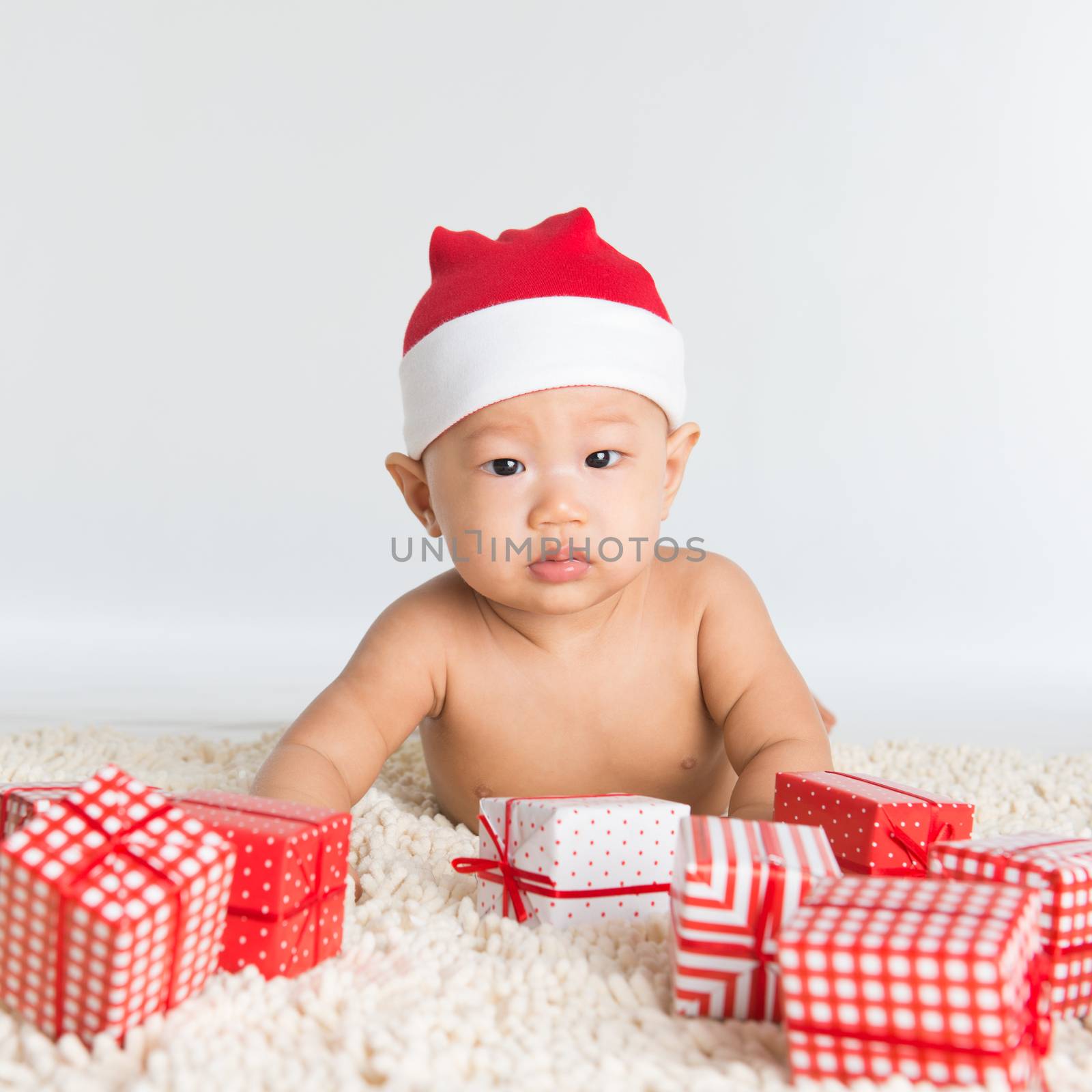 Asian santa hat baby boy with Christmas present on floor.