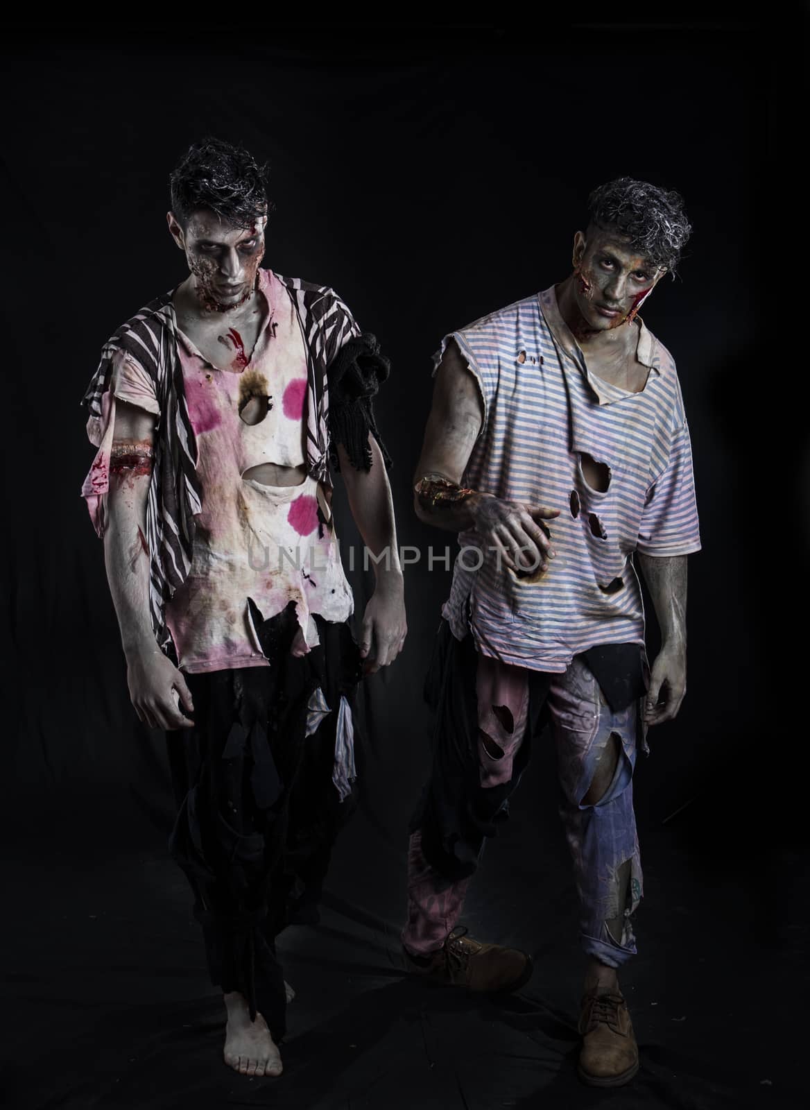 Two male zombies standing on black background walking towards camera