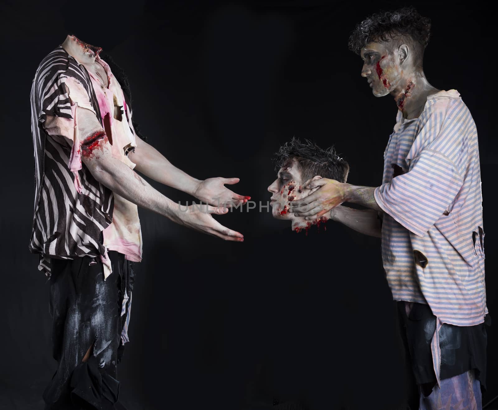 Two male zombies, one giving the head to the decapitated one's body, standing on black background