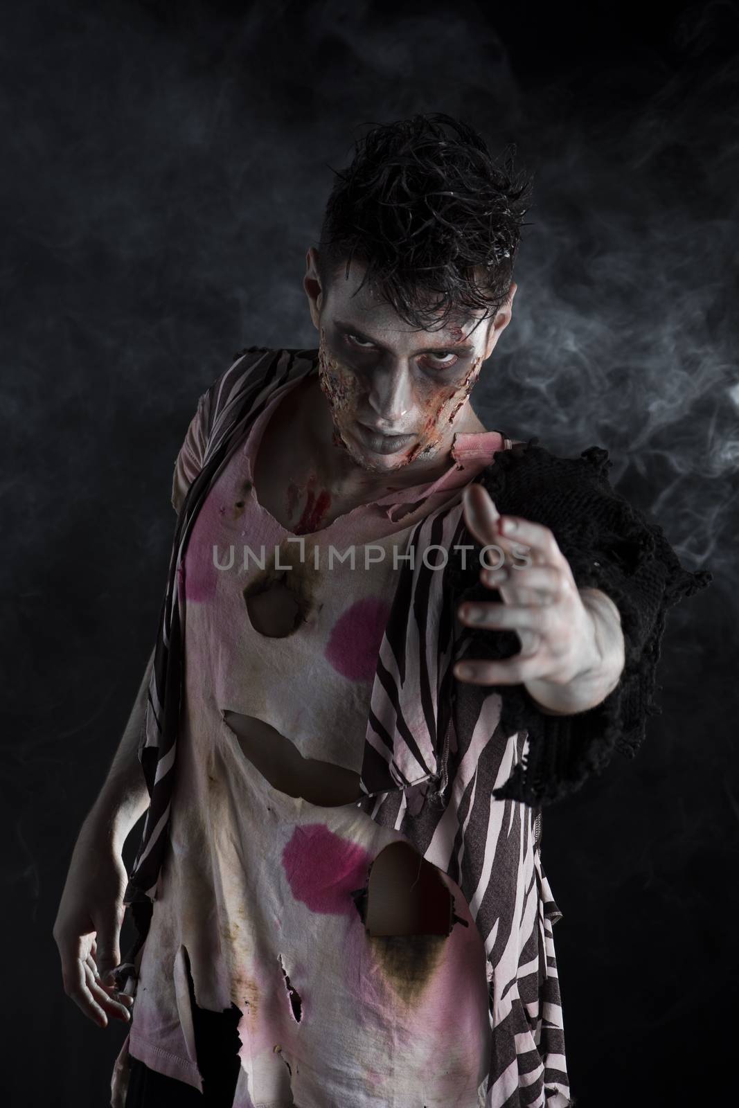 Male zombie standing on black smoky background, reaching hand towards camera