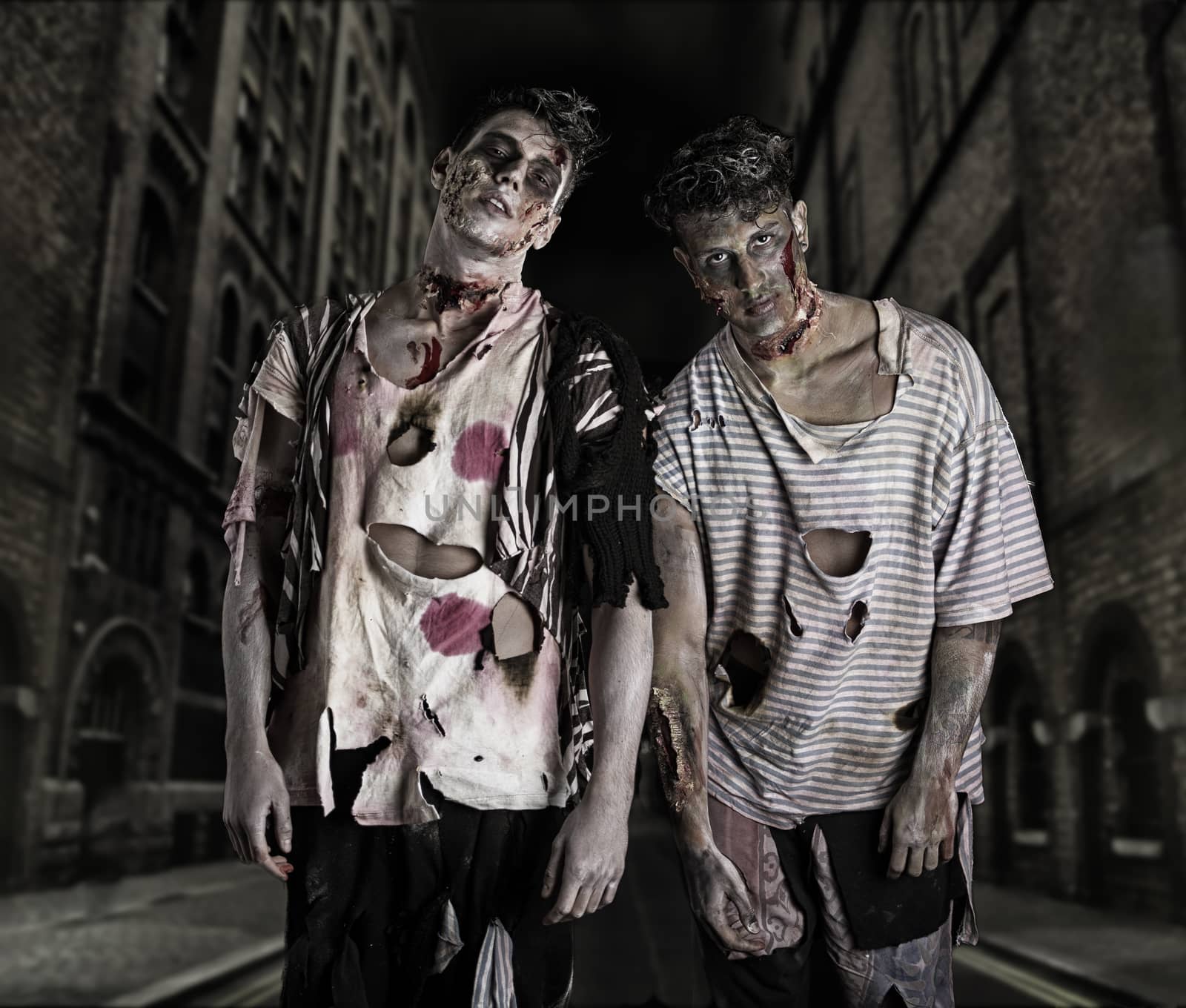 Two male zombies standing in empty city street at night looking at camera. Halloween theme