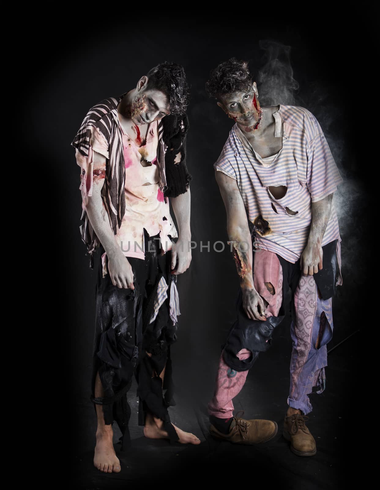 Two male zombies standing on black background, full body shot, looking at camera. Halloween theme